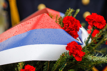 Shallow depth of field (selective focus) image with the Russian flag colored flowers on a funeral wreath with the Russian flag on it during a rainy day.