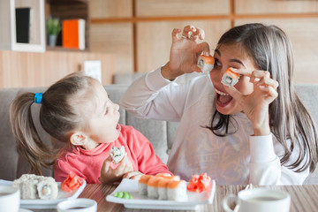 Funny mom with daughter holding sushi rolls in front of eyes