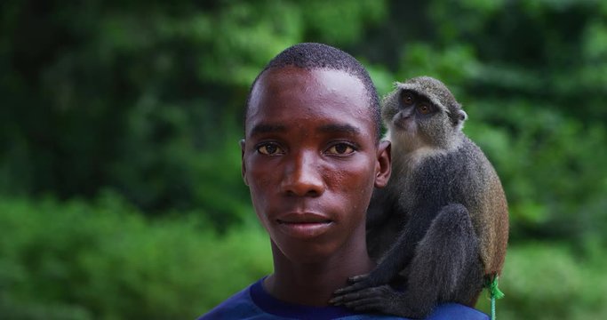 Authentic portrait of happy rural african young guy with a monkey on a shoulder is smiling in camera on a village background. Concept: charity, people,life, happiness, authenticity, love for animals