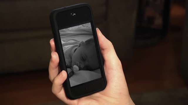 A smartphone device showing a sleeping baby on monitor. Virtual assistant/smarthome concept.  	