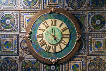 Fototapeta na wymiar Ceramic wall clock with roman dial against the background of ancient fireplace tiles.