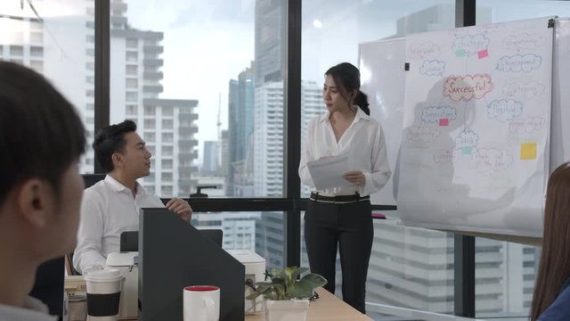 Young asian business woman presenting data idea marketing on board in office. Asia woman show mind mapping and ideas to business partner or colleagues group enjoy teamwork in small office