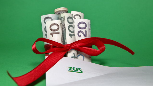 Banknotes of Polish zloty in rolls tied with red ribbon like a gift present next to page of paper with logo ZUS - Polish national social security system, close up on green background