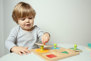 Beautiful toddler play with a wooden frame puzzle geometric figure toys at home. Toddler play with a color educational toy.  Child play at the table in the baby room. Child development.  Funny baby. 