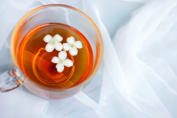 a large mug of tea with fallen white jasmine flowers on a white airy background