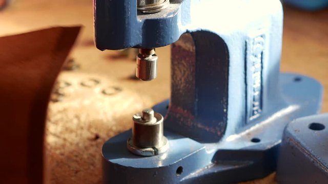 Female craftsman using press for installing metal eyelet on geniune leather product. Close up