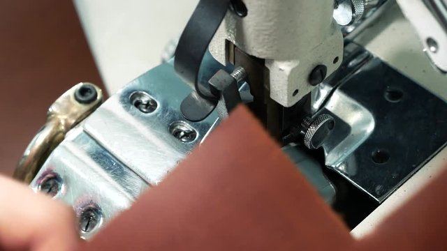 Worker using an automatic leather skiving machine. Skiving leather in a haberdashery manufactory. Splitting, aligning and cutting edge of leather details. Close up