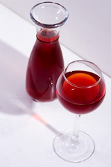 red wine in a wineglass and decanter with shadows isolated on white stone background