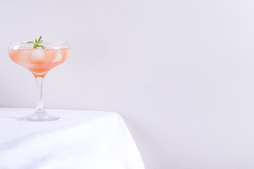 Pink cocktail with rosemary and ice in glass on a white tablecloth on the table