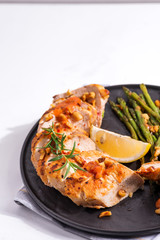 grilled chicken breast fillet with asparagus and lemon in slate plate and white stone background