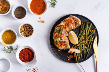 grilled chicken breast fillet with asparagus, sauce, spices and lemon in slate plate and white stone background