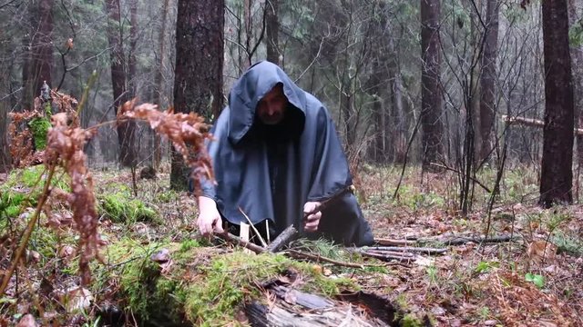 A monk in a black robe lays out wood for a fire in the forest