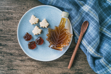 Maple syrup top view of organic natural product from Canada. Maple leaf shape bottle, soft candy and hard candy taffy on rustic wooden kitchen table and spoon for cooking