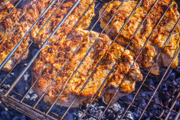 Grilled meat in barbecue with flames and coals. Grilled meat concept.  Few pieces of slightly burnt meat on charred grate with fire and smoke below.  Frying pork on a skewer over a brazier.