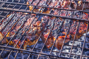 Grilled meat in barbecue with flames and coals. Grilled meat concept.  Few pieces of slightly burnt meat on charred grate with fire and smoke below.  Frying pork on a skewer over a brazier.
