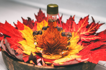 Maple syrup bottle in red maple tree leaves for tourist gift souvenir. Canada grade A amber sweet liquid from Quebec sugar shack. - obrazy, fototapety, plakaty