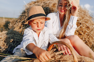 pretty blond long-haired woman with little blond son at sunset relaxing in the field and savoring fruit from a straw basket. summer, farming, nature and fresh air in the countryside.