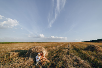Fototapeta premium pretty blond long-haired woman with little blond son at sunset relaxing in the field and savoring fruit from a straw basket. summer, farming, nature and fresh air in the countryside.