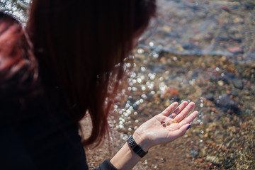 Girl collects stones on the seashore. Young woman looking for beautiful shells in the sand near the water