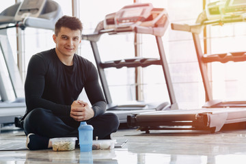 stylish guy in the gym relaxing on the floor and eating healthy food.