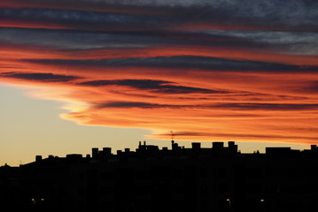 Silueta de edificios al amanecer bajo una capa de nubes estratos anaranjadas