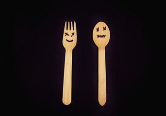 Eco wooden cutlery fork and spoon with creative faces on a black background.