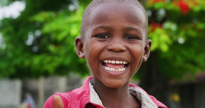Authentic portrait of cute happy rural african toddler boy is smiling in camera on a village background. Concept: charity, people,life, happiness, authenticity