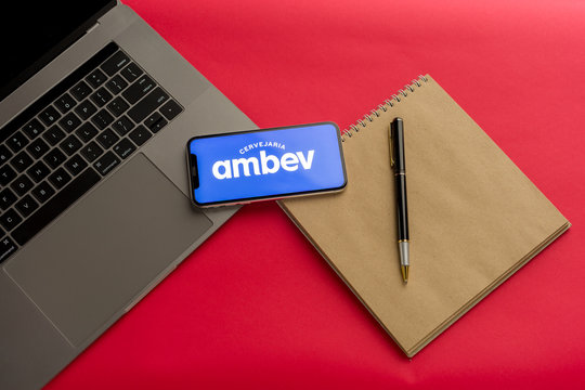 Tula, Russia - February 07, 2020: Logo ambev on a smartphone near modern laptop on red background
