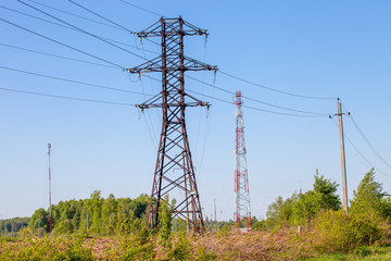 Many power poles, wires, communication towers, antennas against the background of spring nature and the blue sky.