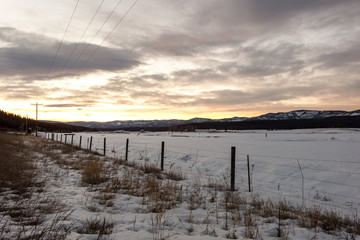 Vintage barb wire fence as leading line past now covered field and long mountain range on cloudy morning