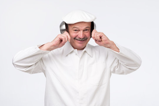 Senior Hispanic Chef Covering His Ears With Cooking Pans Over White Background