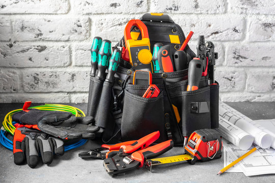 Electrician's tools in a black construction bag on a gray table against a white brick wall. Construction tools of an installer or electrician. Space for text