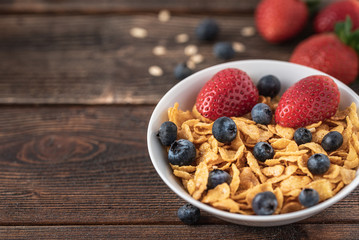 hips with blueberries and raspberries in white bowl in dark wooden desk.
