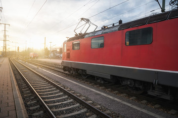 Red locomotive on railway tracks in german train station at sunset