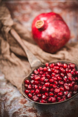 Close Up of Pomegranate Seeds on Old Ladle Sitting on a Tin Tile; Whole Pomegranate in Background