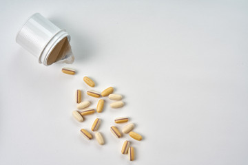 Colored pills scattered from a white bottle on a grey background. Vitamins spilled out of a lying bottle. Top view