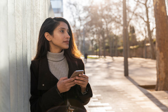 Young woman with smartphone in the city looking around