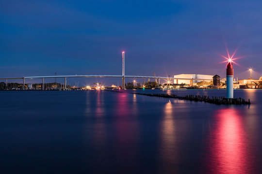 Germany, Mecklenburg-Western Pomerania, Stralsund, Lighthouse at end of pier at dusk with?Rugen Bridge in background