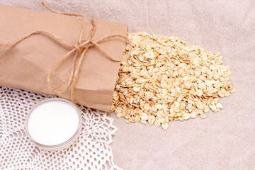dry natural oat flakes. Oatmeal from an ecological paper bag. Natural linen background with eco bag and oatmeal flakes. A cup of milk