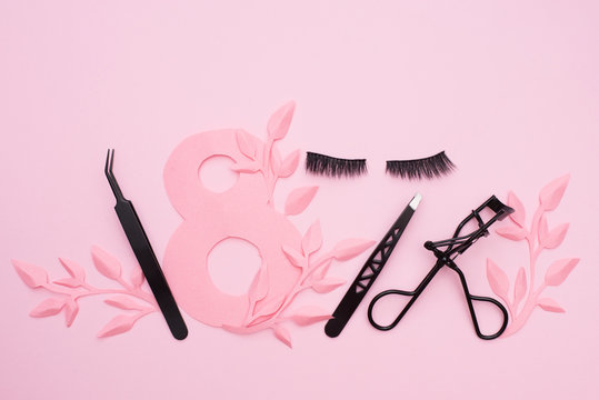 false eyelashes and black tweezers on pink backdround with paper leaves, copy space. World Women's Day, March 8th