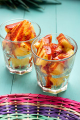 Pineapple cutted with chili powder and piquant sauce in glass on turquoise background