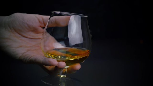 Slow motion footage of cognac or whiskey in a glass, alcohol tasting, glass of golden spirits in a hand