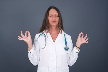 Meditation, religion and spiritual practices. Beautiful young doctor female doing yoga in the morning before work, keeping eyes closed, holding fingers in mudra gesture.