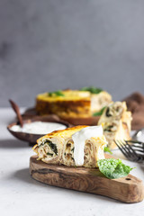 Crepes roll with spinach, chicken and cream cheese baked with bechamel sauce on a wooden plate,...