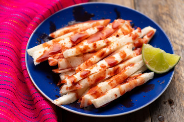 Mexican jicama  cutted with chili powder and piquant sauce on wooden background