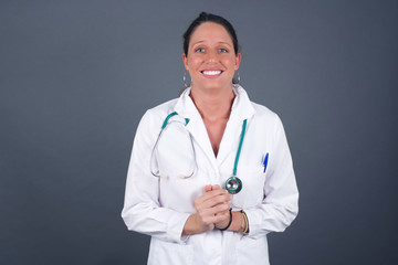 Wow. Beautiful doctor female isolated on gray studio background. Young emotional surprised woman standing with open mouth. Human emotions, facial expression concept. Trendy colors.