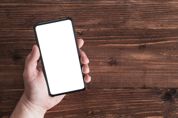 male left hand holding smartphone with white screen on brown wooden background