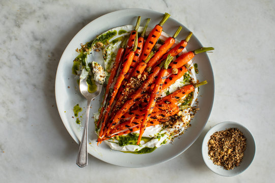 Overhead view of grilled carrots served with hazelnut dukkah, yogurt and carrot top oil on plate