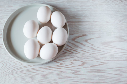 Easter white eggs on ceramic plate on white wooden table. Top view of easter background.