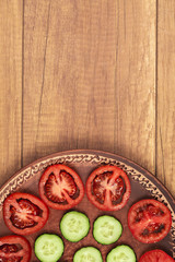 sliced tomatoes and cucumbers in a clay brown plate on a wooden table. top view